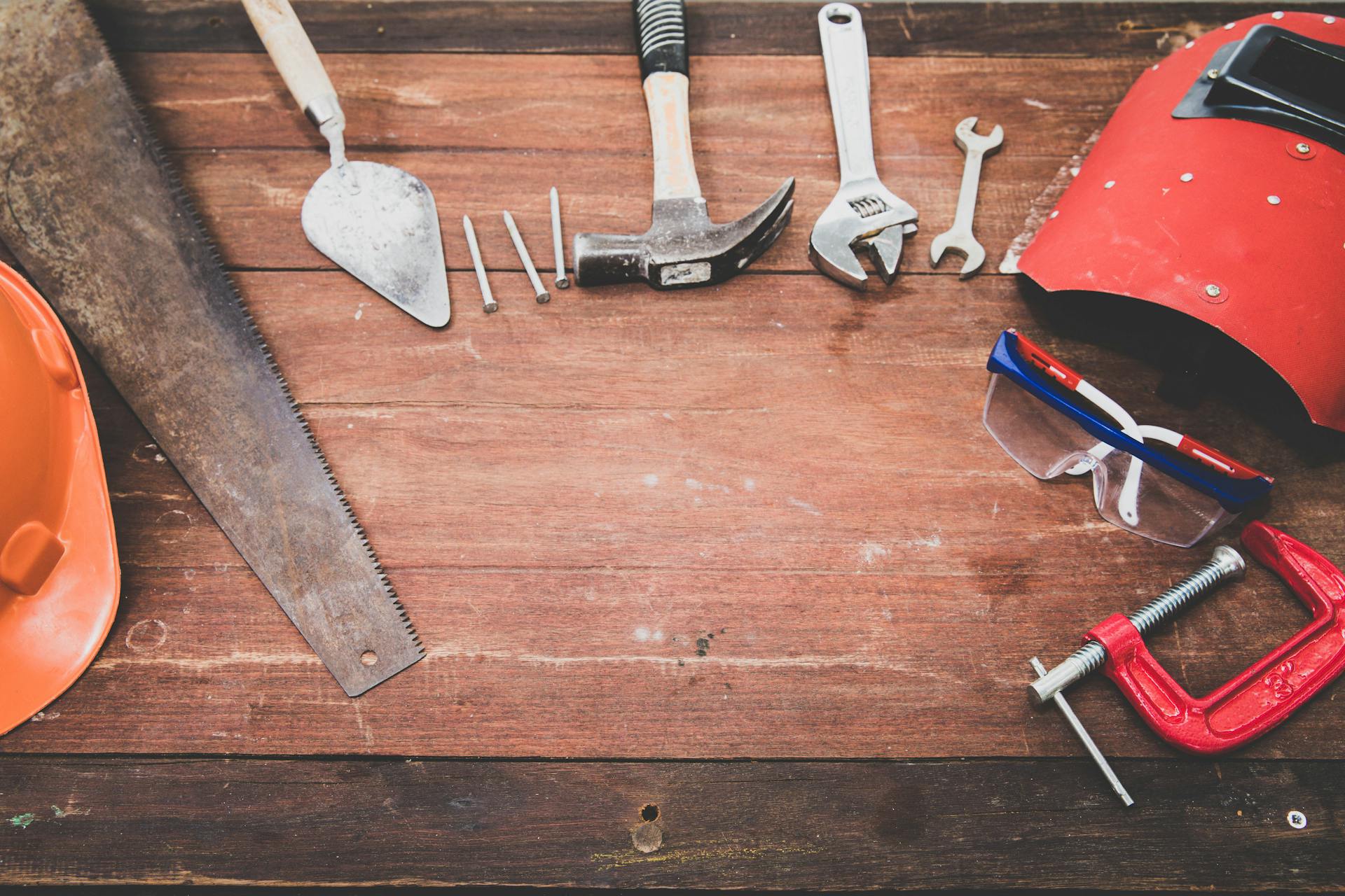 A table containing a saw, builder's trowel, nails, a hammer, an adjustable spanner, a regular spanner, a protective mask and a vice.