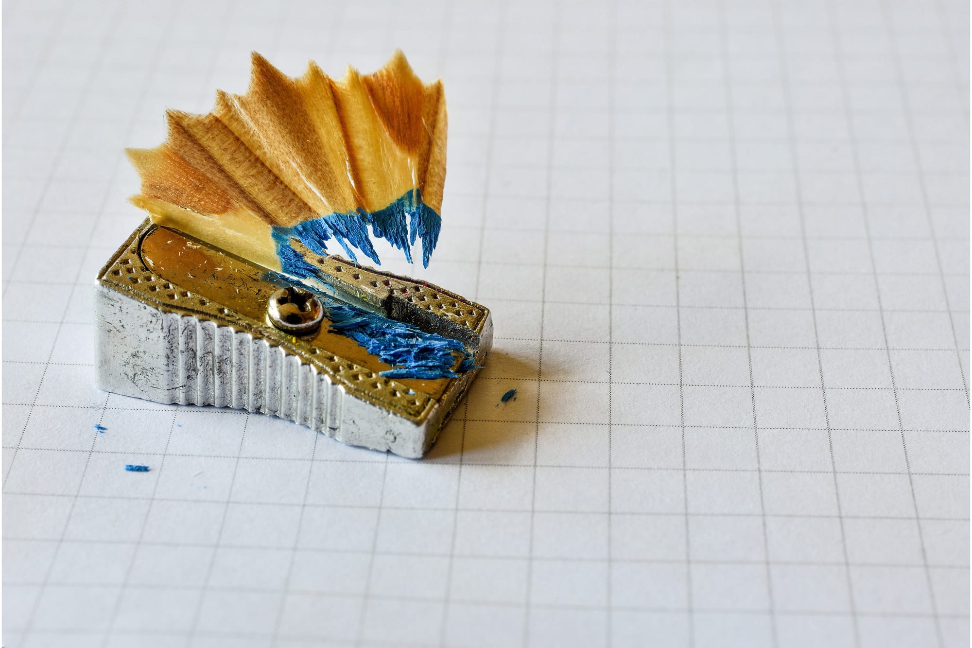 A small, metal pencil-sharpener with the shavings of a blue pencil.