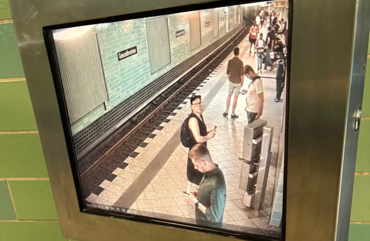 A photograph of Kim (the author) watching themselves on a black and white CCTV screen on the Berlin subwa